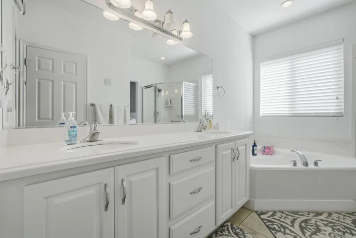 Full bath featuring double vanity, light tile patterned floors, a garden tub, and a stall shower