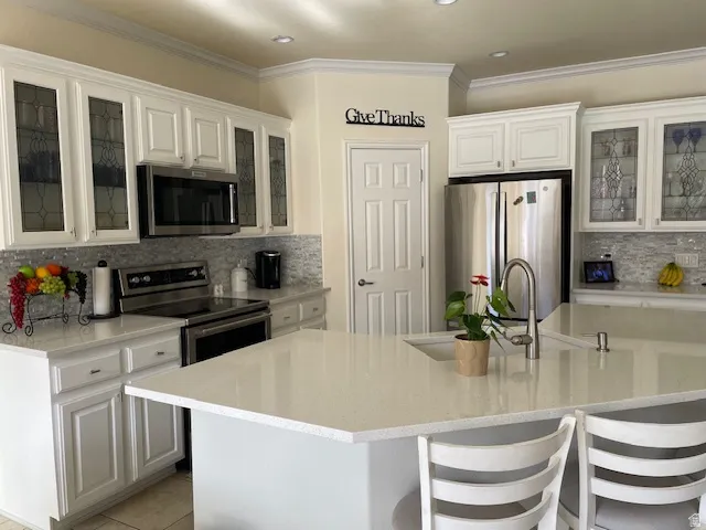 Kitchen with glass fronted cabinets, stainless steel appliances, decorative backsplash, white cabinets, and ornamental molding