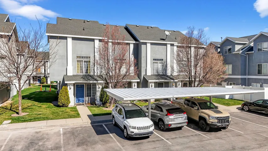 View of front of house with covered and uncovered parking, a front yard, and stucco siding