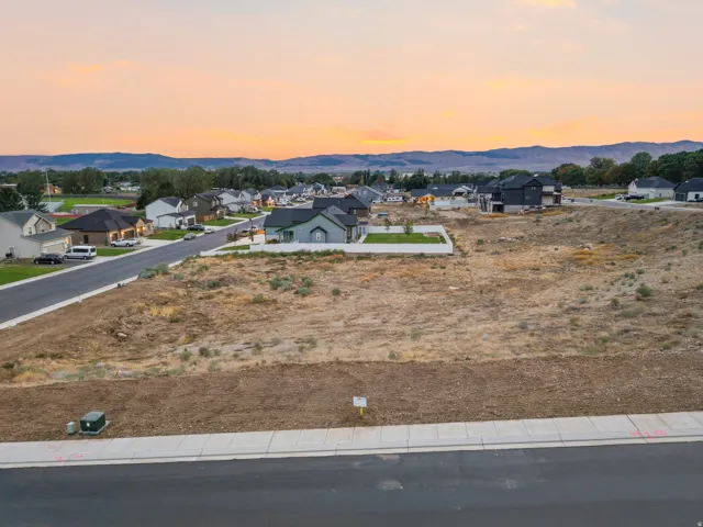 Expansive undeveloped lot featuring paved road access, concrete sidewalk, and surrounding residential properties