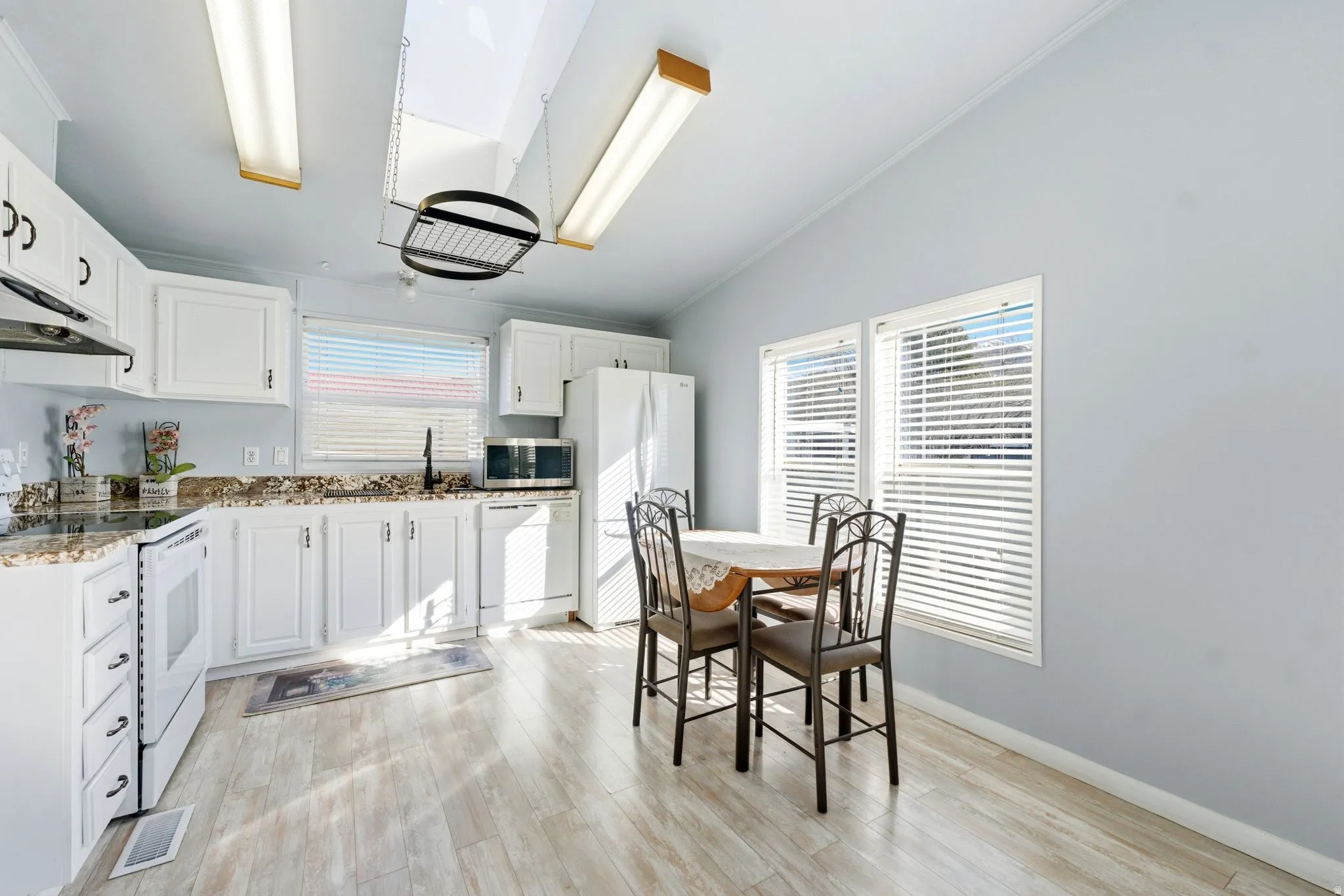 Kitchen featuring white appliances, white cabinets, light wood-type flooring, lofted ceiling, and ornamental molding