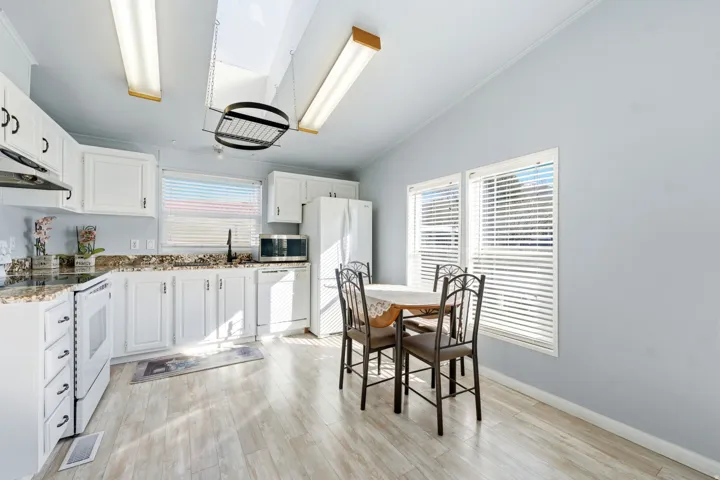 Kitchen featuring white appliances, white cabinets, light wood-type flooring, lofted ceiling, and ornamental molding