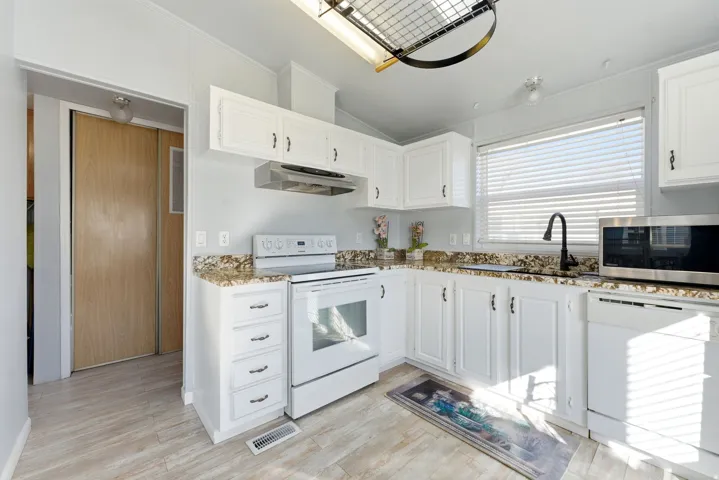 Kitchen with white appliances, white cabinetry, crown molding, light wood-type flooring, and lofted ceiling