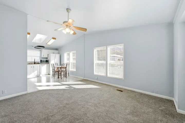 Living room featuring ceiling fan, light colored carpet, lofted ceiling, and a skylight