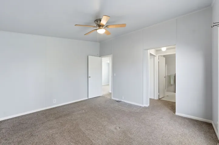 Unfurnished bedroom with carpet floors, ceiling fan, ensuite bath, and ornamental molding
