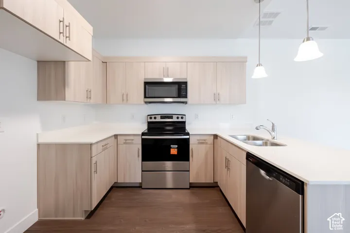 U-shaped kitchen featuring light wood-finish cabinetry, solid surface countertops, stainless steel appliances, and pendant lighting