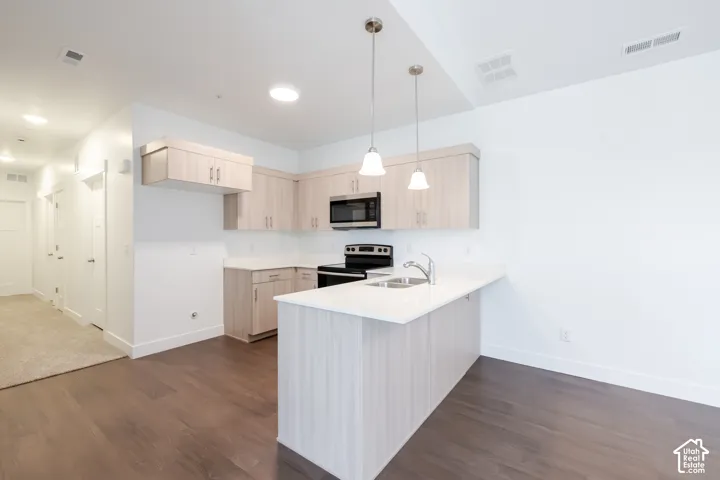 Modern kitchen featuring light wood-finish cabinetry, stainless steel appliances, a white countertop, and two pendant lights