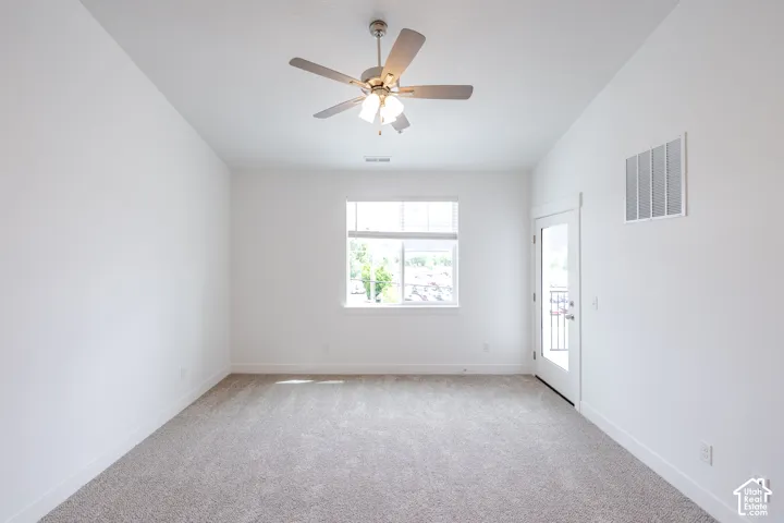 Bright room with neutral carpet flooring, a ceiling fan, a large window, and a glass-paneled door