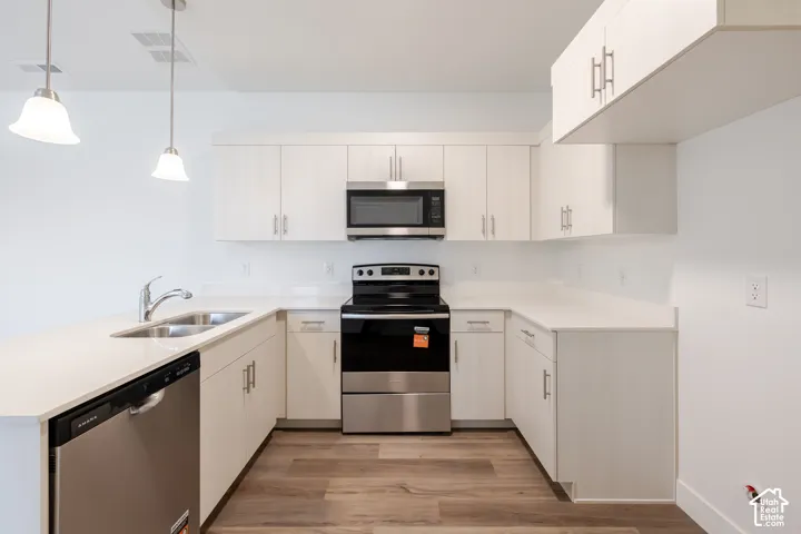 U-shaped kitchen featuring white cabinetry, stainless steel appliances, pendant lighting, and wood-finish flooring