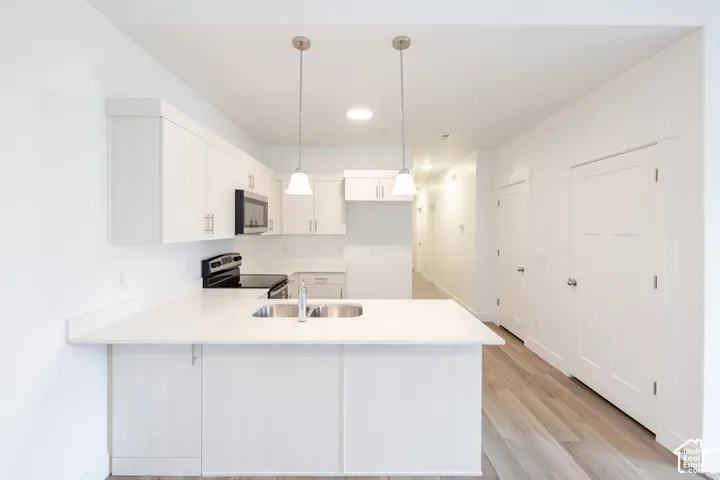 Bright kitchen featuring white cabinetry, a built-in microwave, a stainless steel sink, pendant lighting, and wood-finish flooring