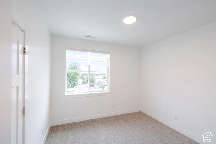 Neutral-toned carpet flooring, white walls, and a large window with white blinds
