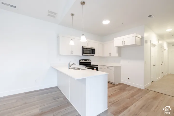 Modern kitchen featuring white cabinetry, a peninsula with a sink, stainless steel appliances, and pendant lighting