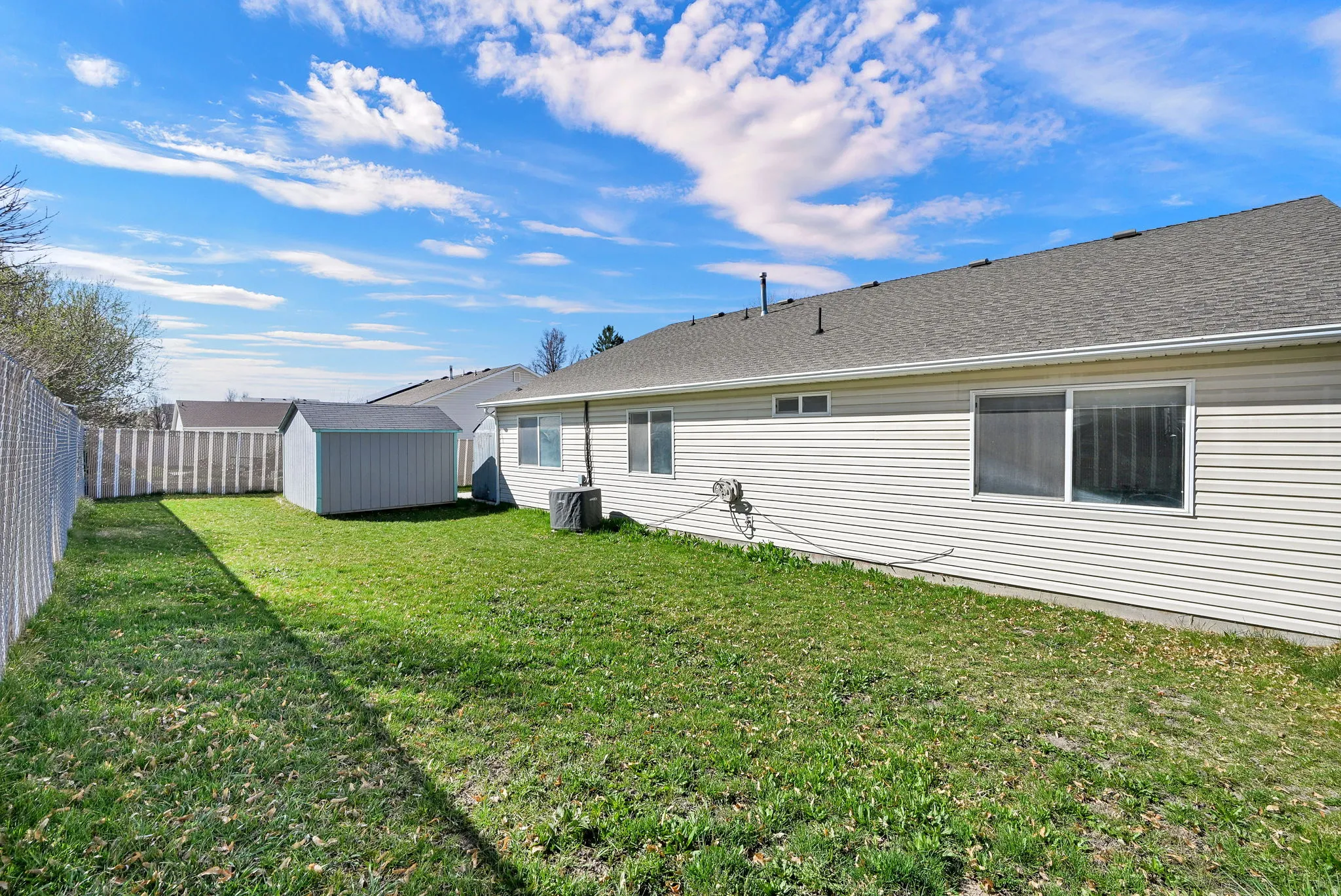 Back of property featuring a storage unit, a fenced backyard, and a shingled roof