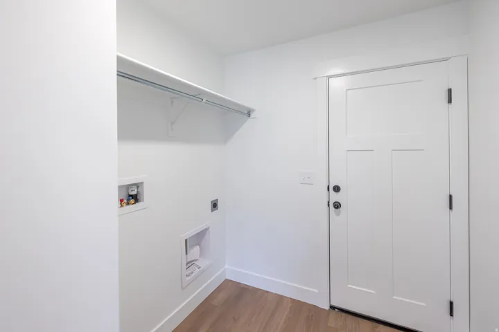 Dedicated laundry area featuring a white shelf with hanging rod, utility hookups, and wood-finish flooring