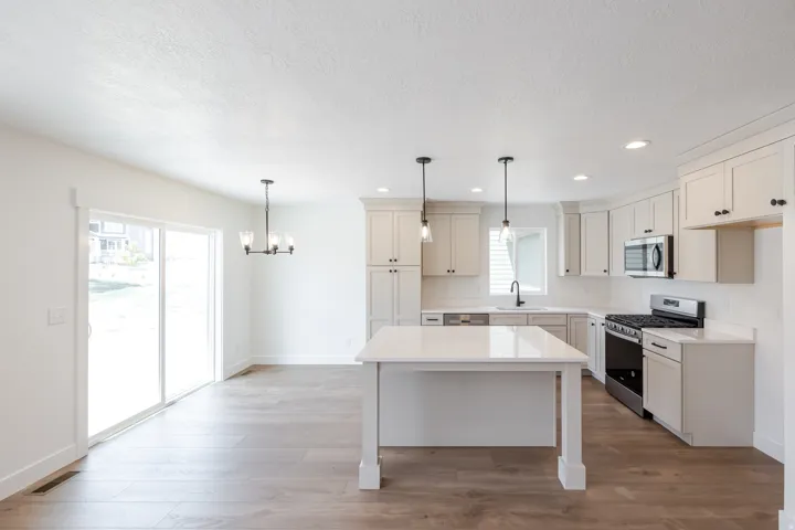 Open-concept kitchen and dining area featuring a central island with a quartz countertop, stainless steel appliances, white cabinetry, and wood-finish flooring