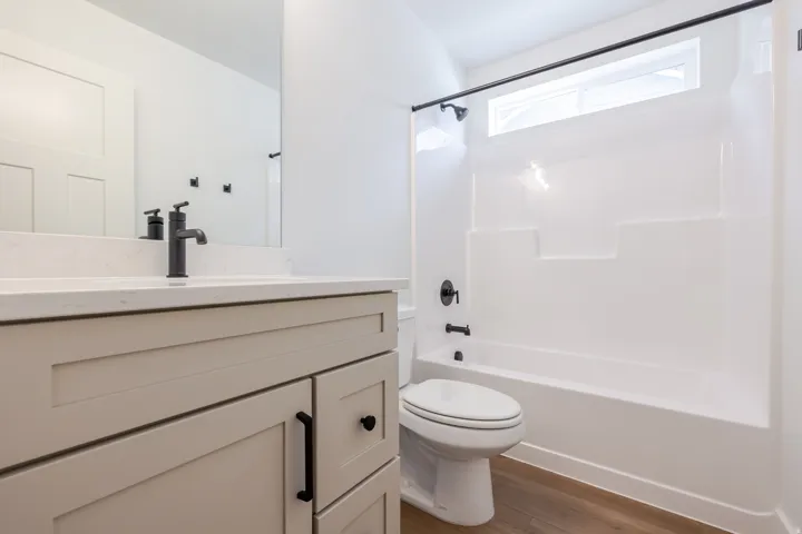 Modern bathroom featuring a white vanity with a quartz-finish countertop, matte black fixtures, a white shower/tub combination, and wood-finish flooring