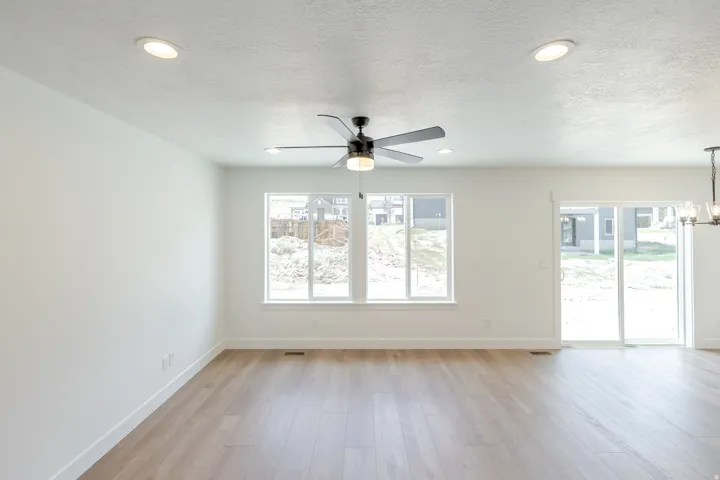 Spacious open-concept room featuring light wood-finish flooring, recessed lighting, and a modern ceiling fan