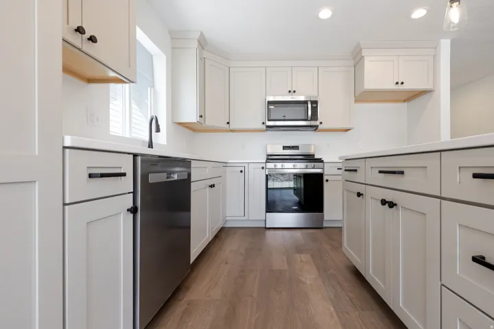 Contemporary kitchen featuring white shaker cabinetry with matte black hardware, white countertops, stainless steel appliances, and wood-finish flooring