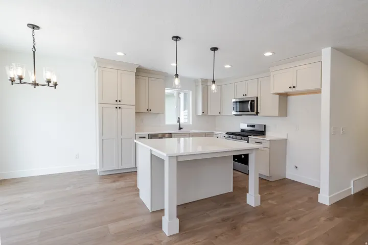 Kitchen featuring an island, light wood-finish flooring, white cabinetry, stainless steel appliances, and recessed lighting