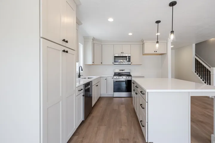 Contemporary kitchen featuring light wood-finish flooring, white cabinetry, integrated stainless steel appliances, a center island with pendant lighting, and recessed ceiling lights