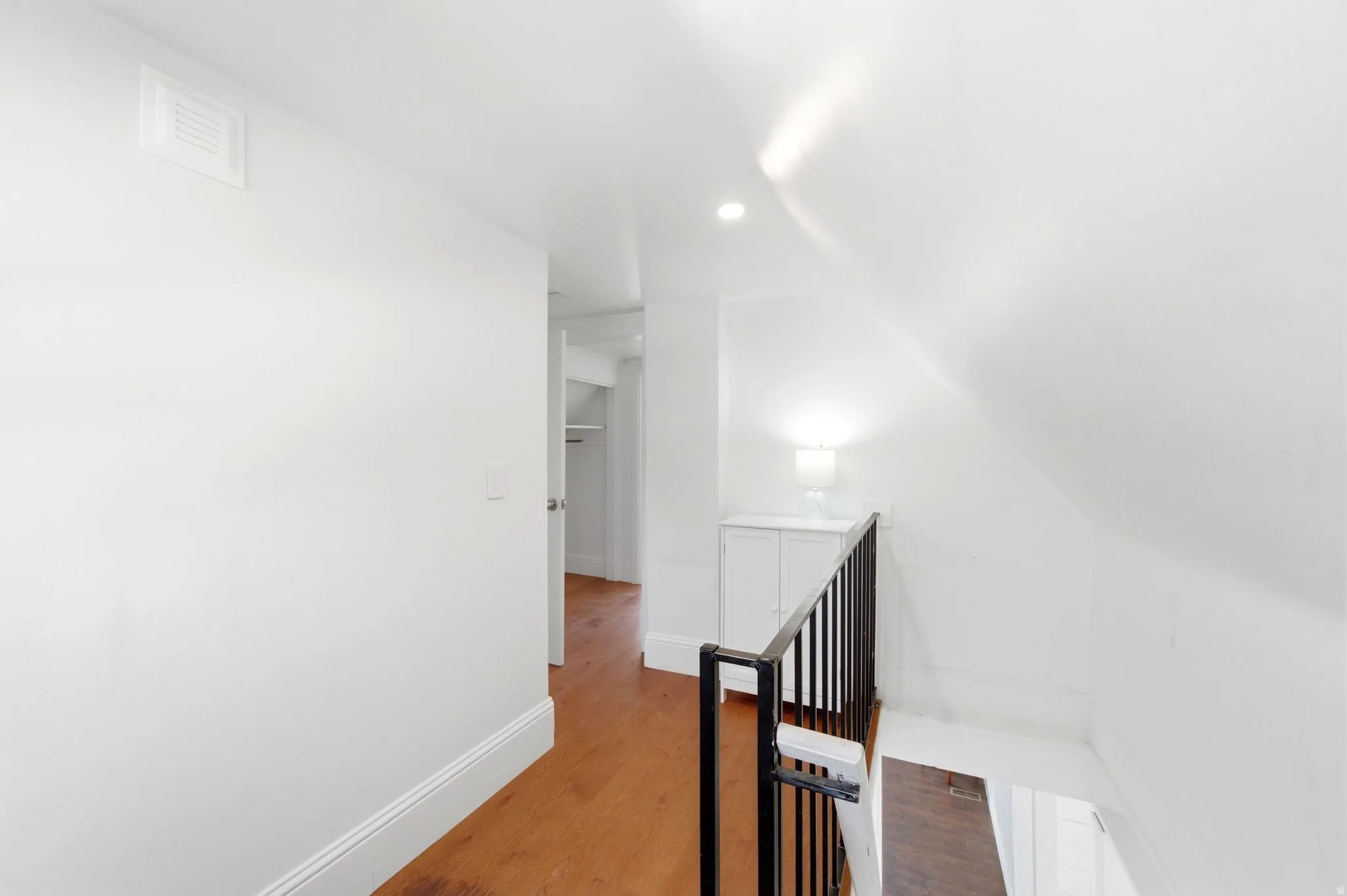 Hall with an upstairs landing, wood finished floors, vaulted ceiling, and recessed lighting