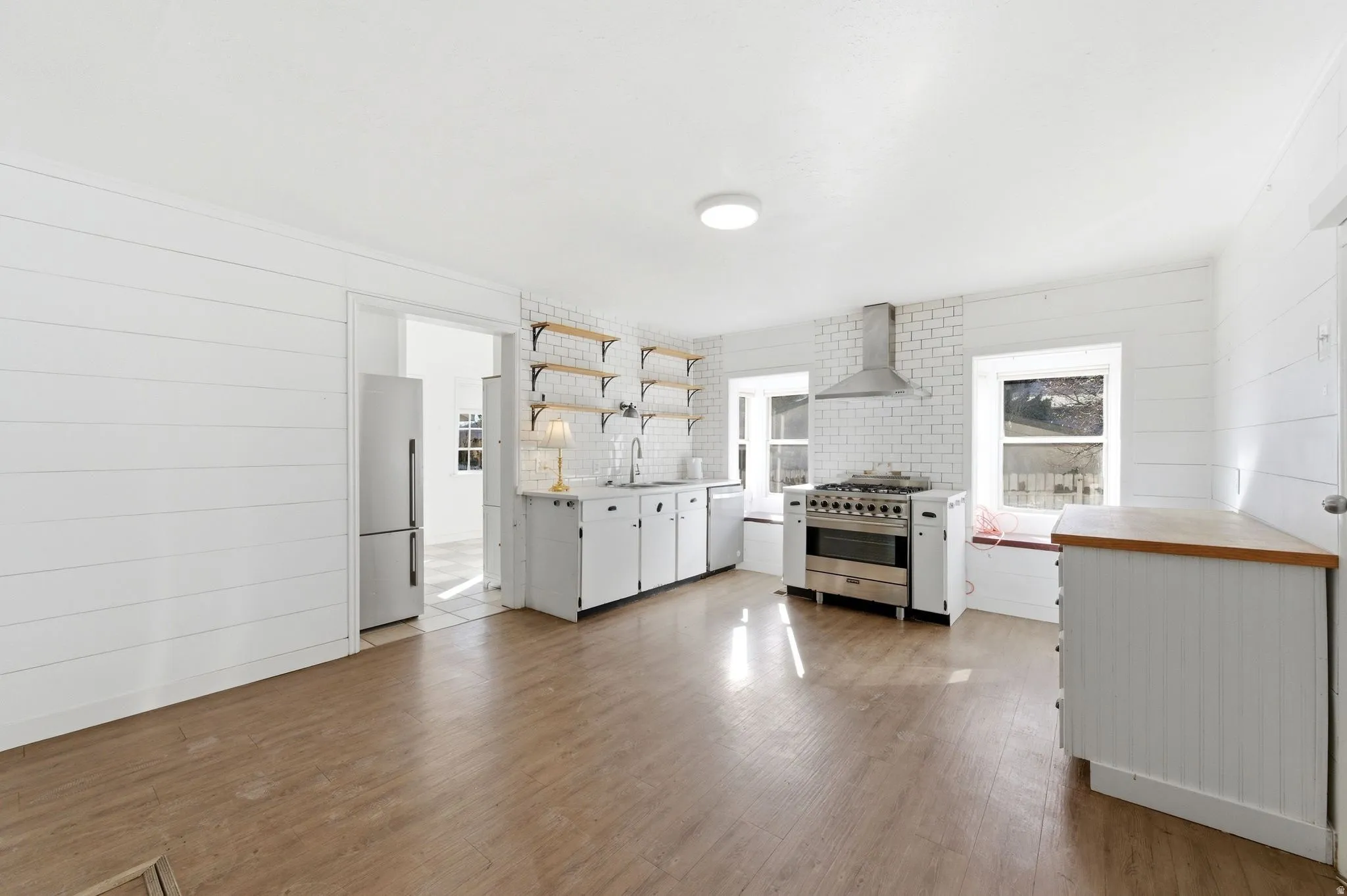 Kitchen featuring white cabinets, stainless steel appliances, open shelves, light wood finished floors, and backsplash