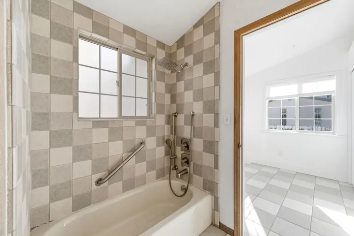 Full bath featuring washtub / shower combination, light tile patterned flooring, and lofted ceiling