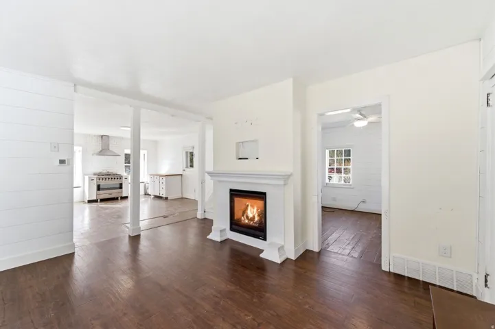 Unfurnished living room with dark wood finished floors, a lit fireplace, a ceiling fan, and wooden walls