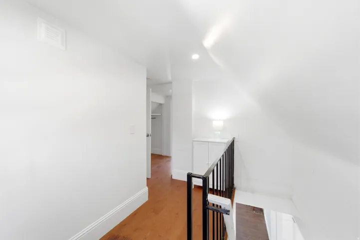 Hall with an upstairs landing, wood finished floors, vaulted ceiling, and recessed lighting
