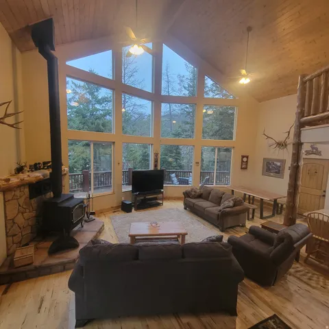 Living area featuring light wood-style floors, a ceiling fan, a wood stove, and a high wood ceiling