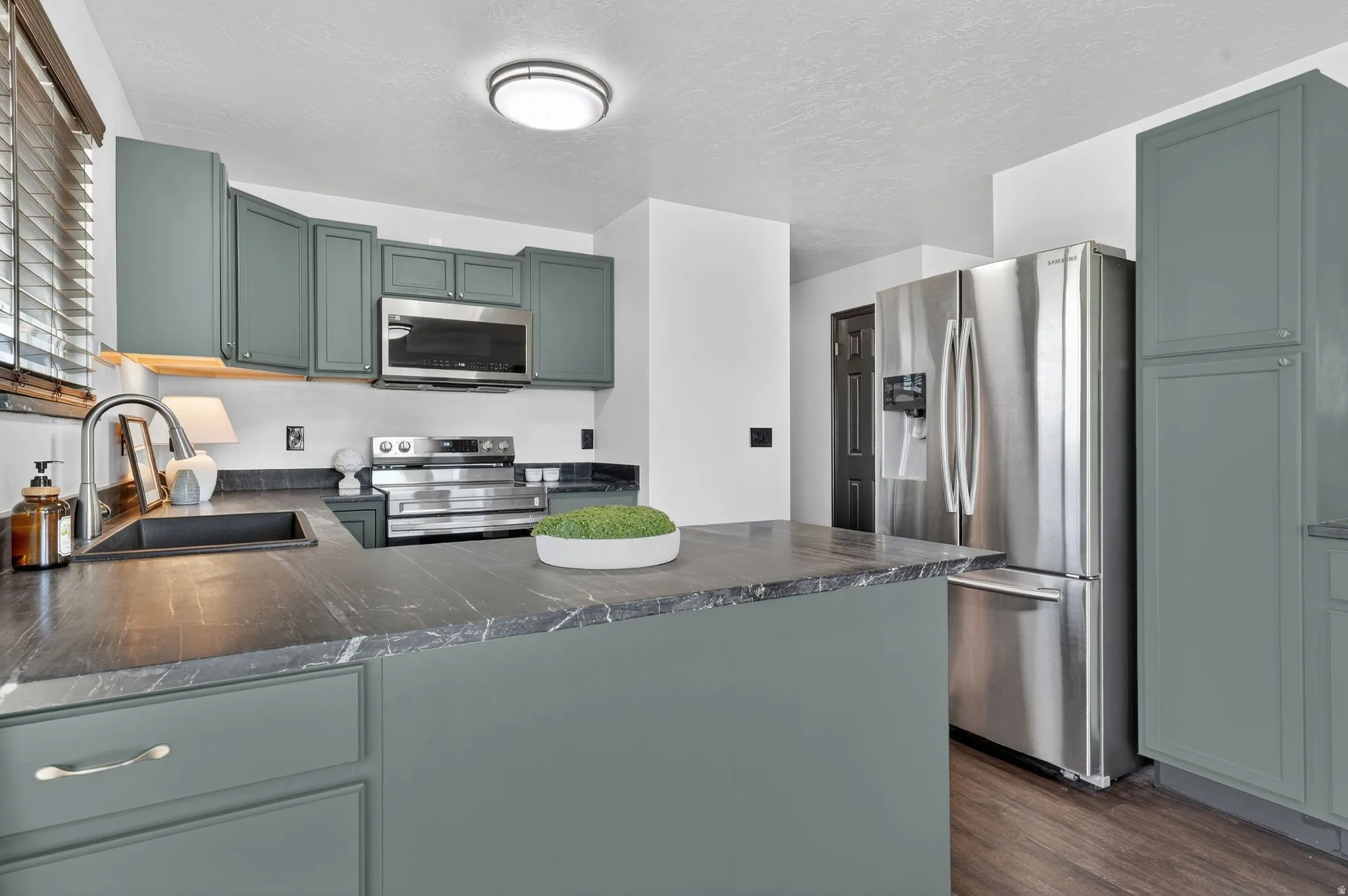Kitchen featuring a peninsula, stainless steel appliances, dark countertops, green cabinets, and dark wood-style floors