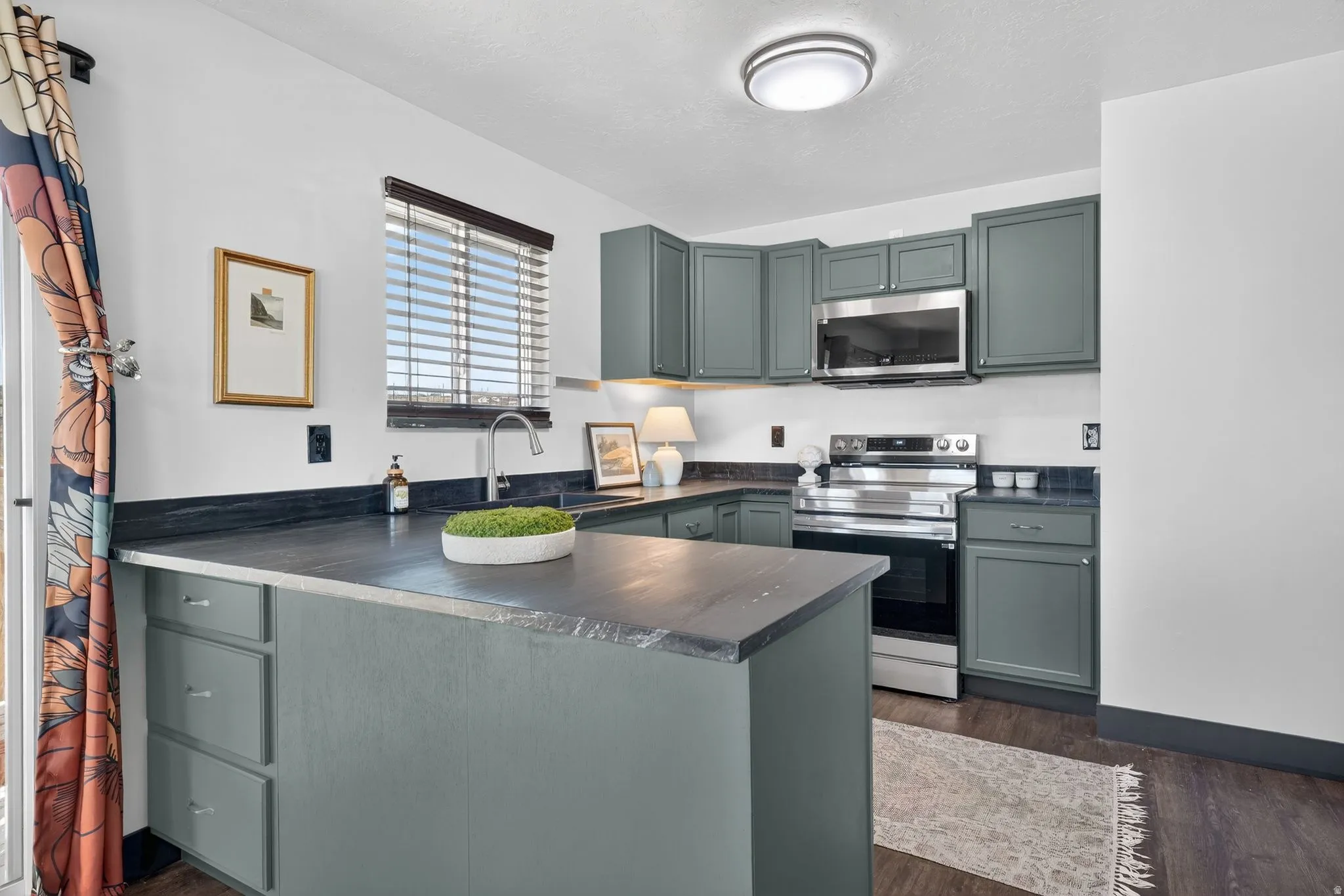 Kitchen featuring stainless steel appliances, dark countertops, a peninsula, dark wood-style flooring, and gray cabinetry