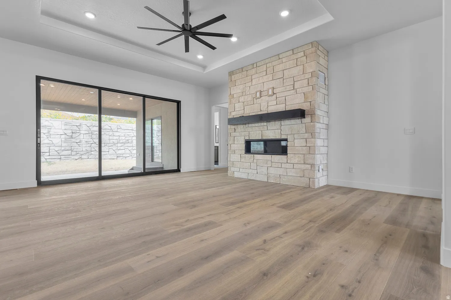 Unfurnished living room with light wood-type flooring, a ceiling fan, a fireplace, a tray ceiling, and recessed lighting