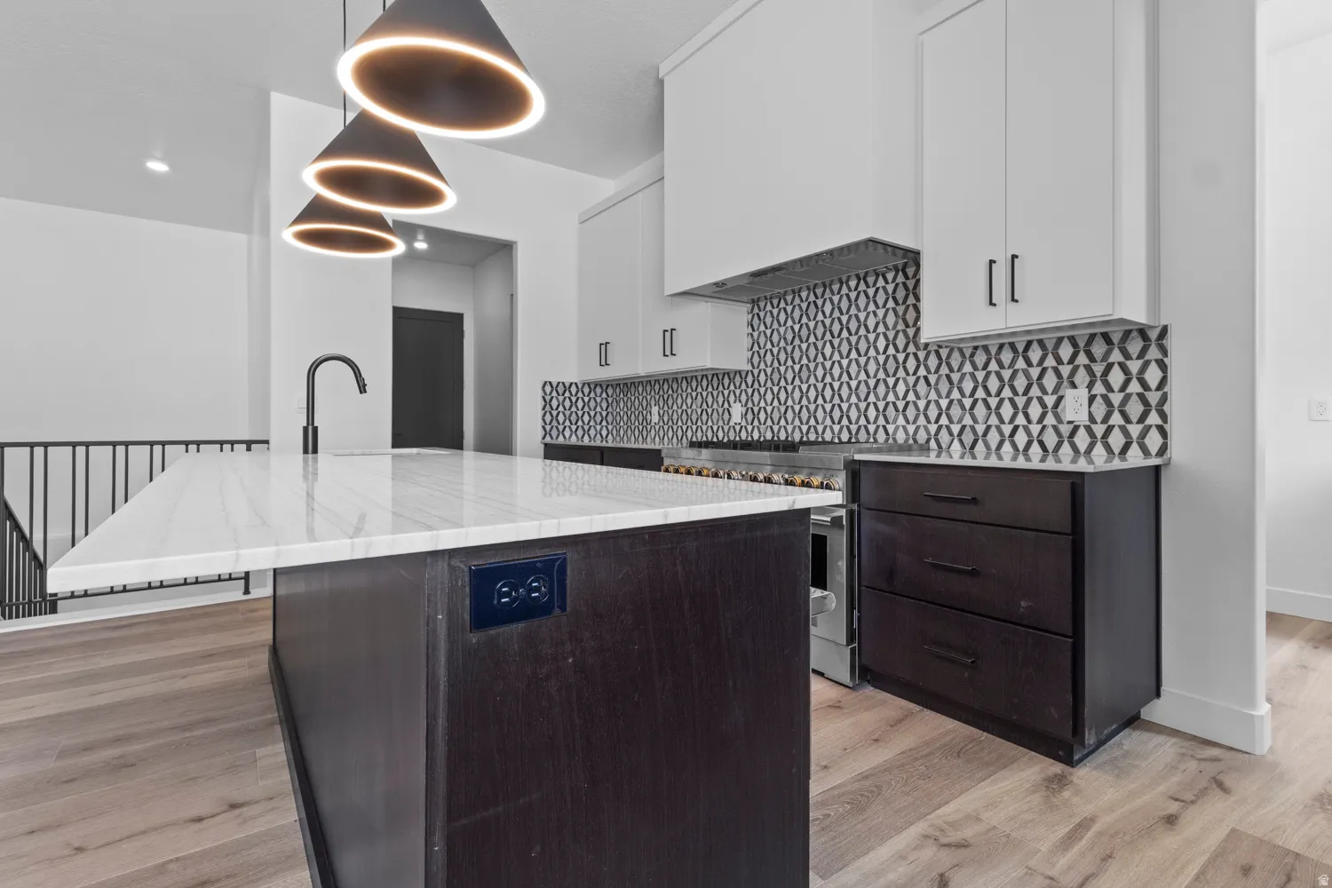 Kitchen featuring two tone cabinets, an island with sink, light stone countertops, high end stove, and light wood-style floors
