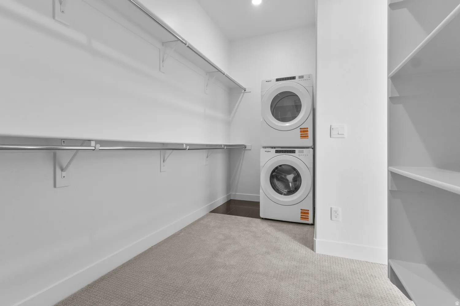 Laundry area with stacked washer and clothes dryer, light carpet, and recessed lighting