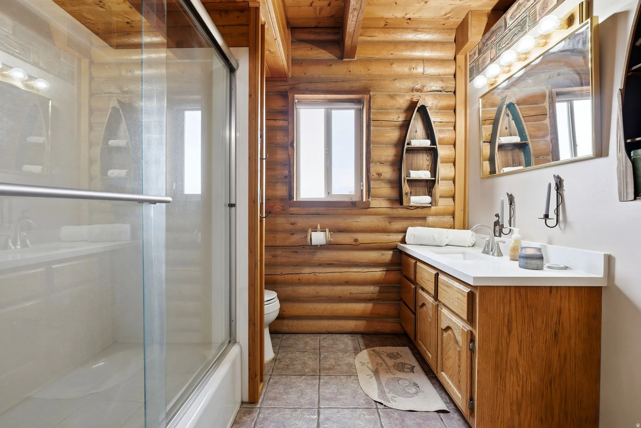Bathroom with rustic walls, vanity, bath / shower combo with glass door, and light tile patterned floors