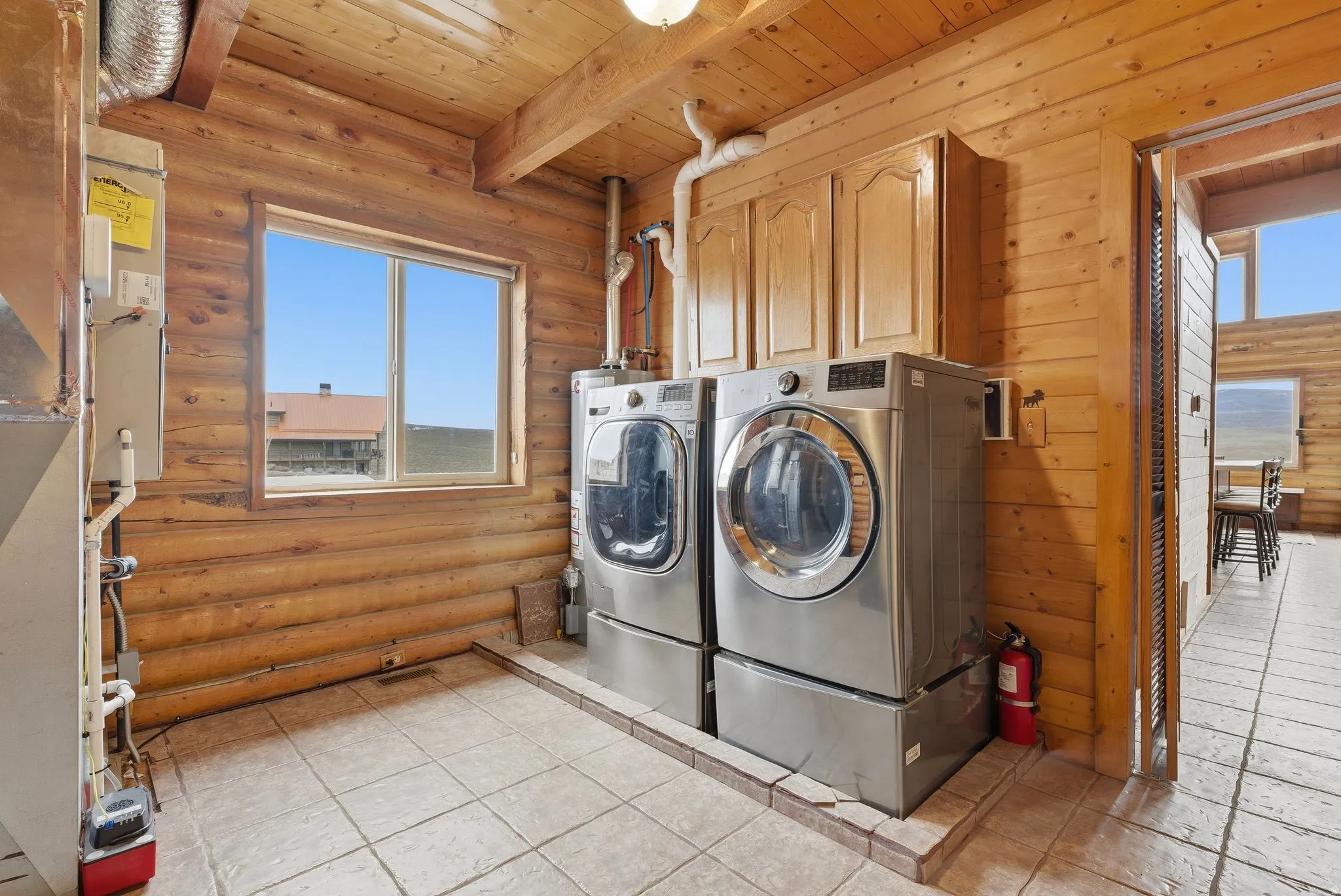 Laundry area with a wooden ceiling with exposed beams, rustic walls, separate washer and dryer, heating unit, and cabinet space