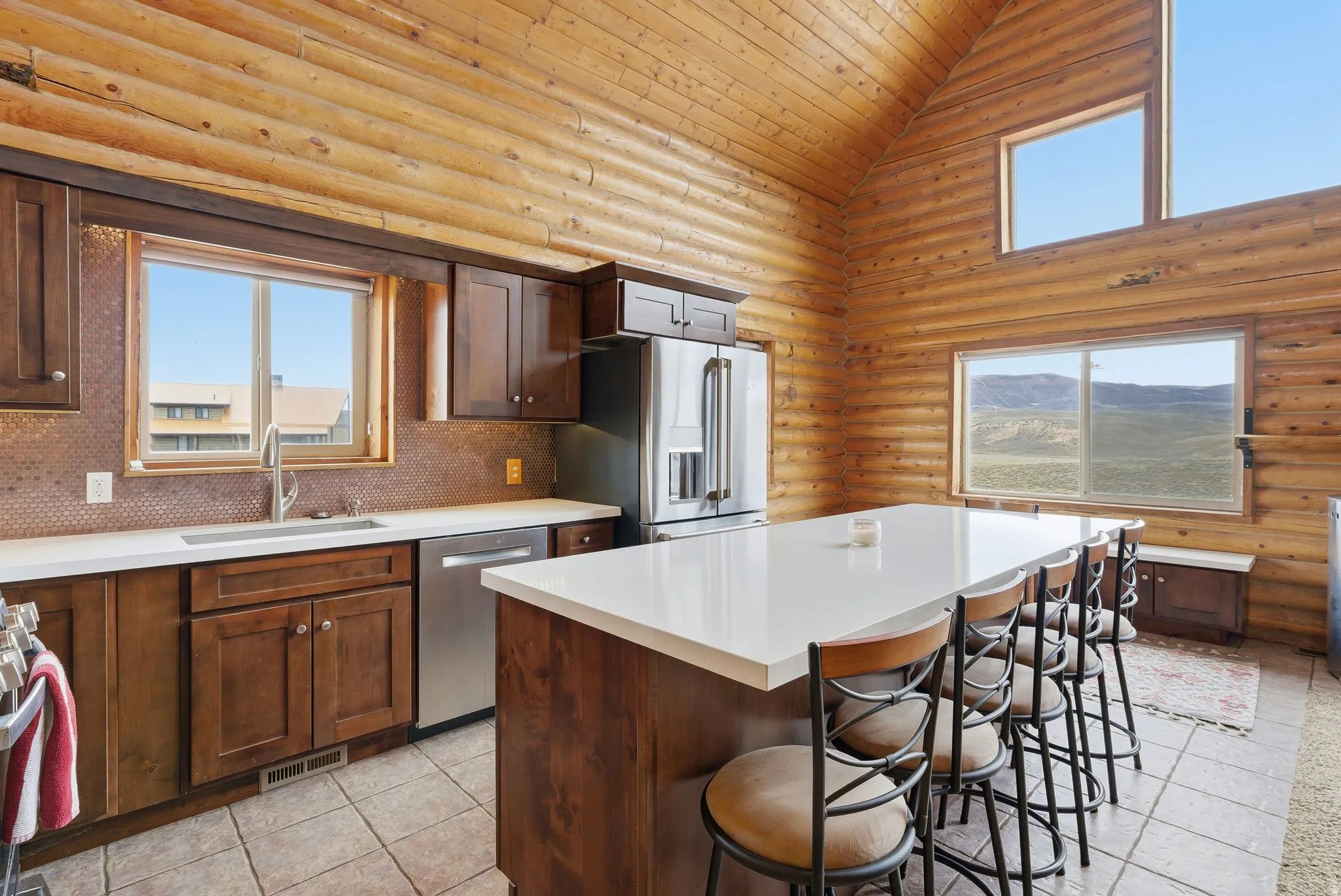 Kitchen with a kitchen bar, rustic walls, stainless steel appliances, a kitchen island, and a vaulted wooden ceiling