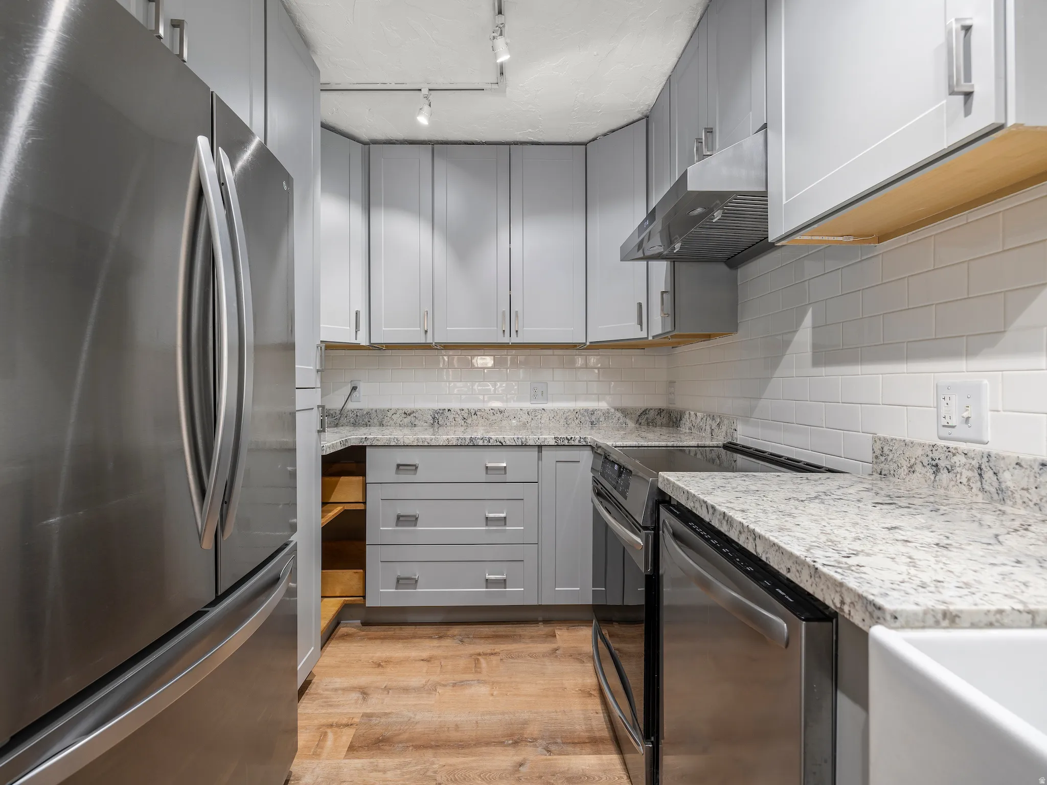 Kitchen featuring gray cabinets, stainless steel appliances, light stone counters, tasteful backsplash, and light wood-type flooring