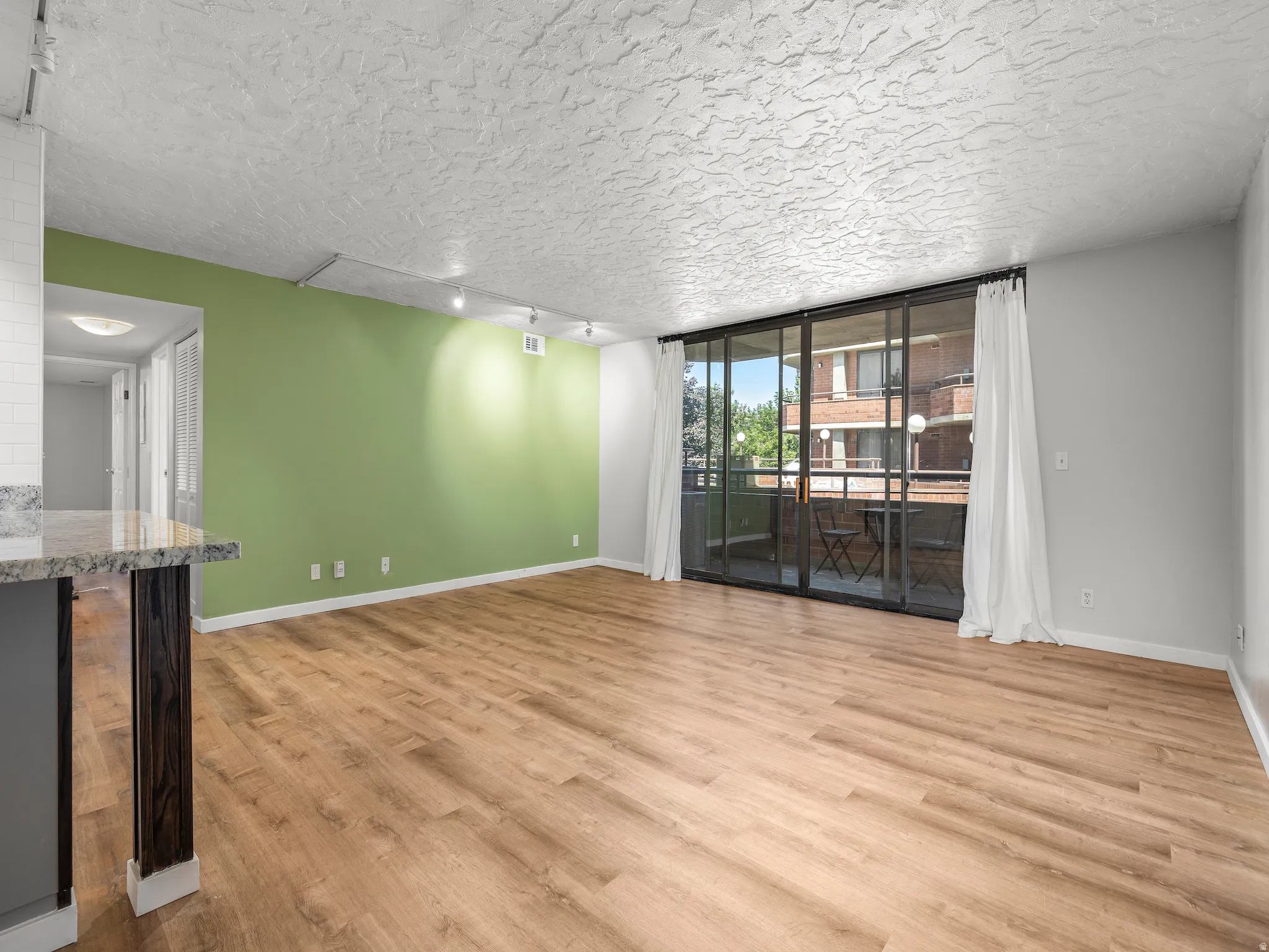Unfurnished room with rail lighting, expansive windows, light wood-style floors, and a textured ceiling