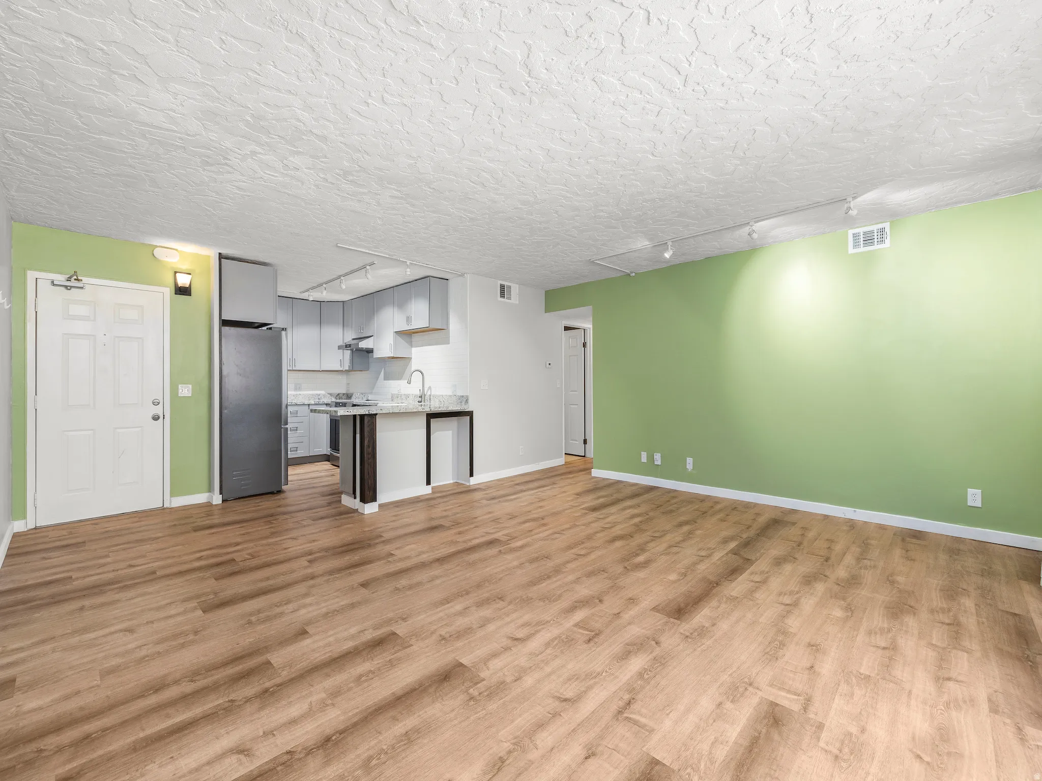 Unfurnished living room with rail lighting, light wood-style flooring, and a textured ceiling