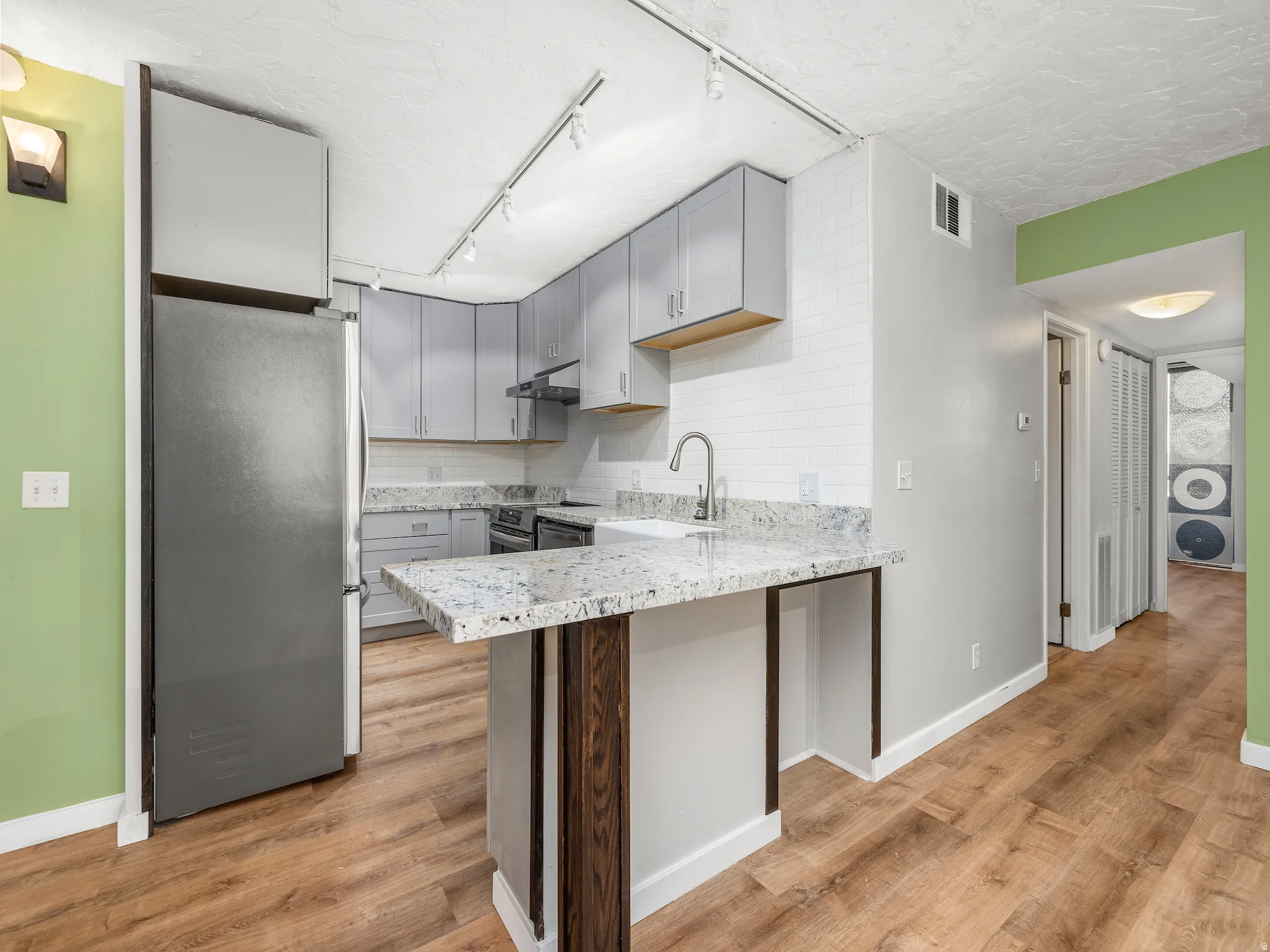 Kitchen with stainless steel appliances, rail lighting, a peninsula, gray cabinetry, and light wood-type flooring