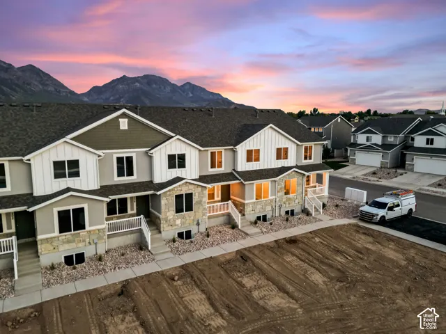 Contemporary townhome exterior featuring stone accents, white vertical siding, dark shingle roofing, and a concrete pathway