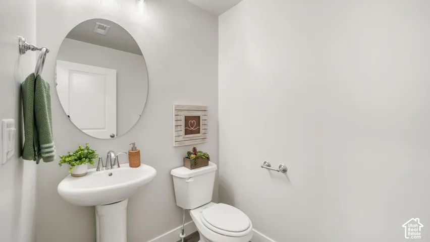 Pedestal sink with chrome faucet, oval mirror, and white toilet