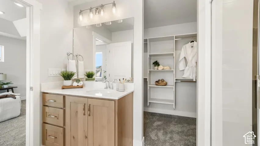Bathroom vanity featuring a light wood-finish cabinet with brushed nickel hardware, a white undermount sink, and a light-toned countertop