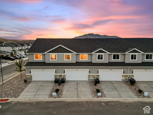 Row of contemporary townhomes featuring gray siding, stone accents, individual garages with white doors, and paved driveways