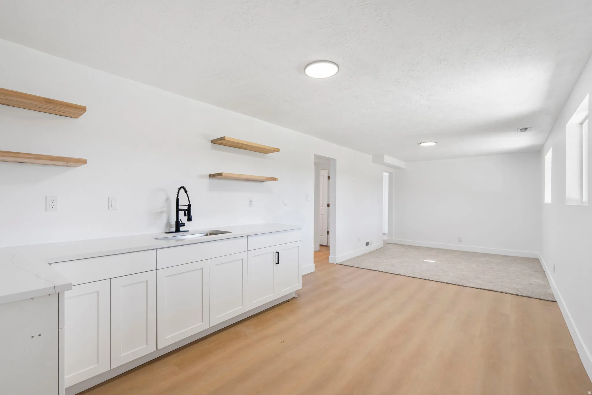 Bar area featuring open shelves, white cabinets, light wood-style flooring, light stone counters, and a textured ceiling