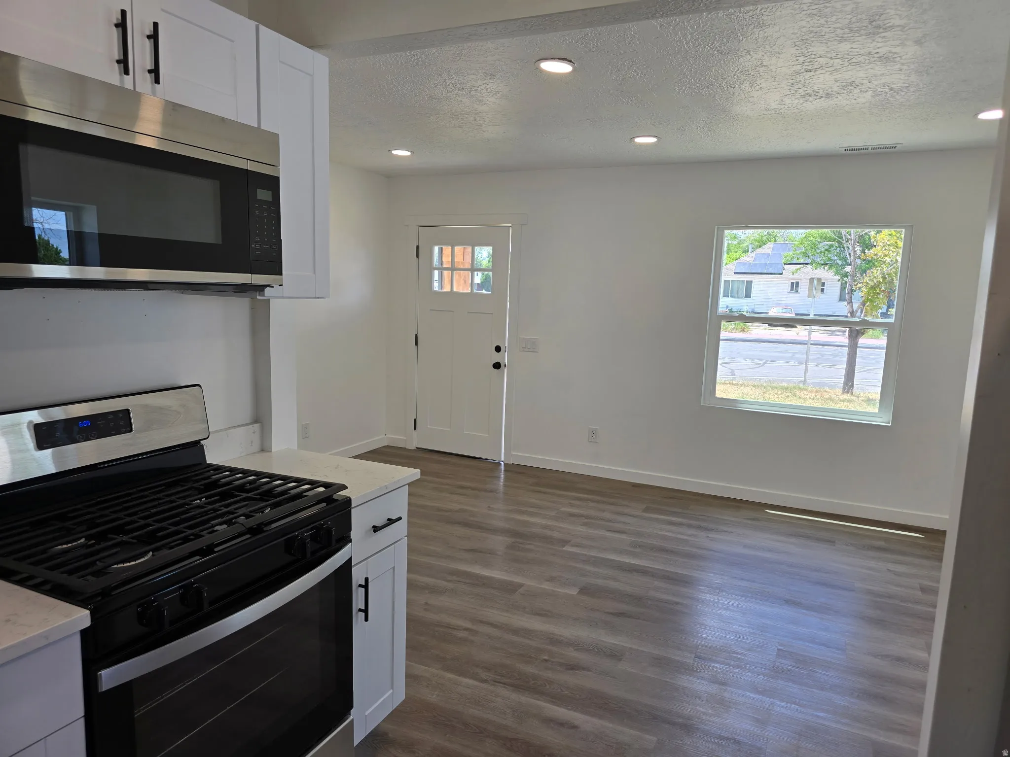 Kitchen with stainless steel appliances, white cabinets, recessed lighting, a textured ceiling, and dark wood-type flooring