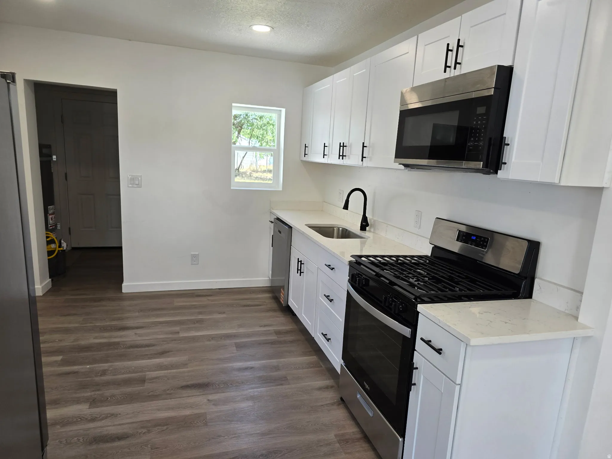 Kitchen featuring stainless steel appliances, white cabinets, light stone counters, dark wood-type flooring, and a textured ceiling