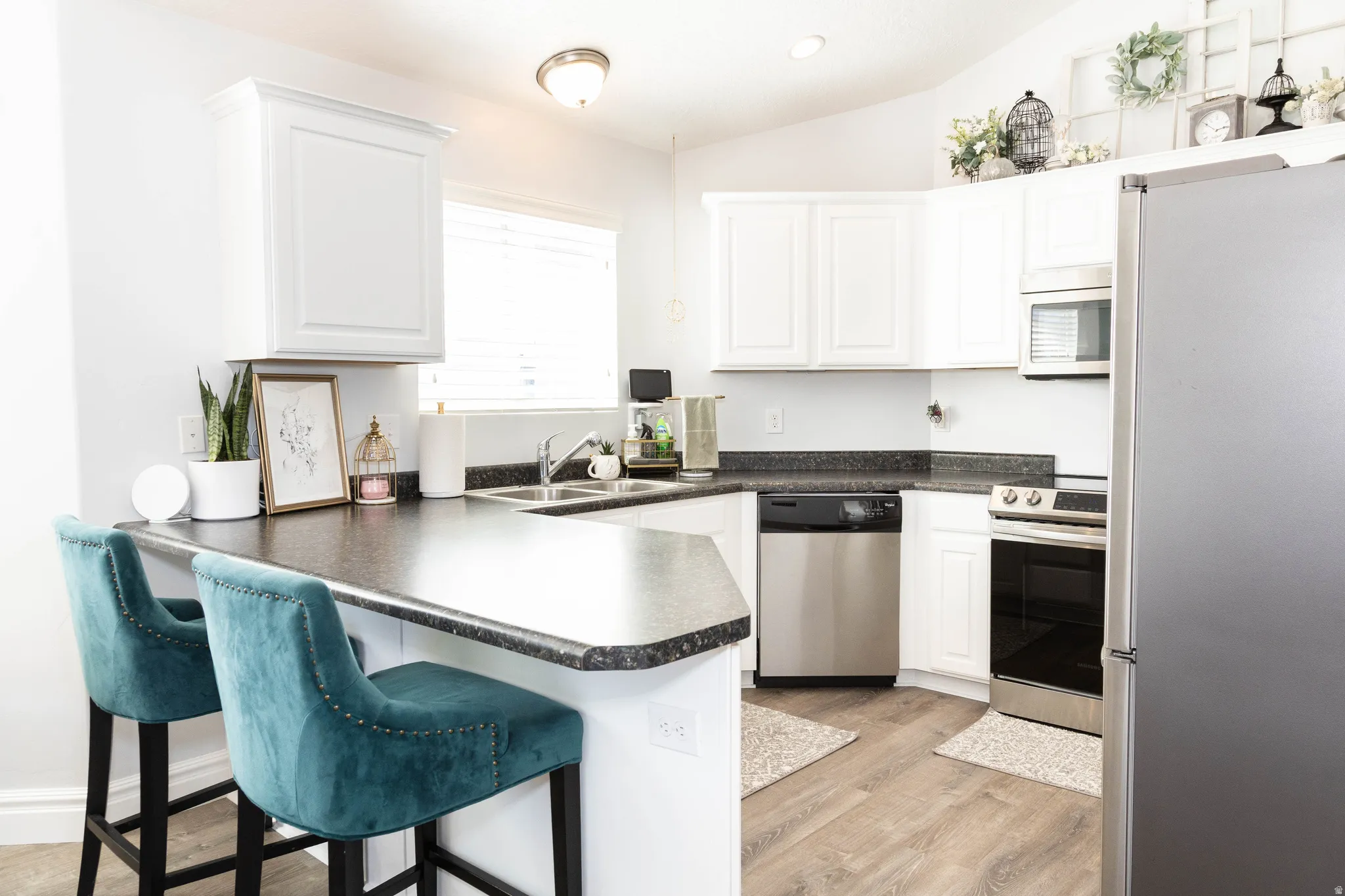 Kitchen featuring dark countertops, stainless steel appliances, a kitchen bar, white cabinetry, and lofted ceiling